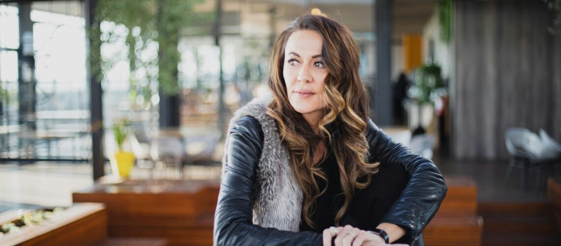 Woman in a leather jacket seated alone at a wooden table, looking away in quiet reflection — representing the emotional reality of codependency.