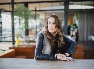 Woman in a leather jacket seated alone at a wooden table, looking away in quiet reflection — representing the emotional reality of codependency.
