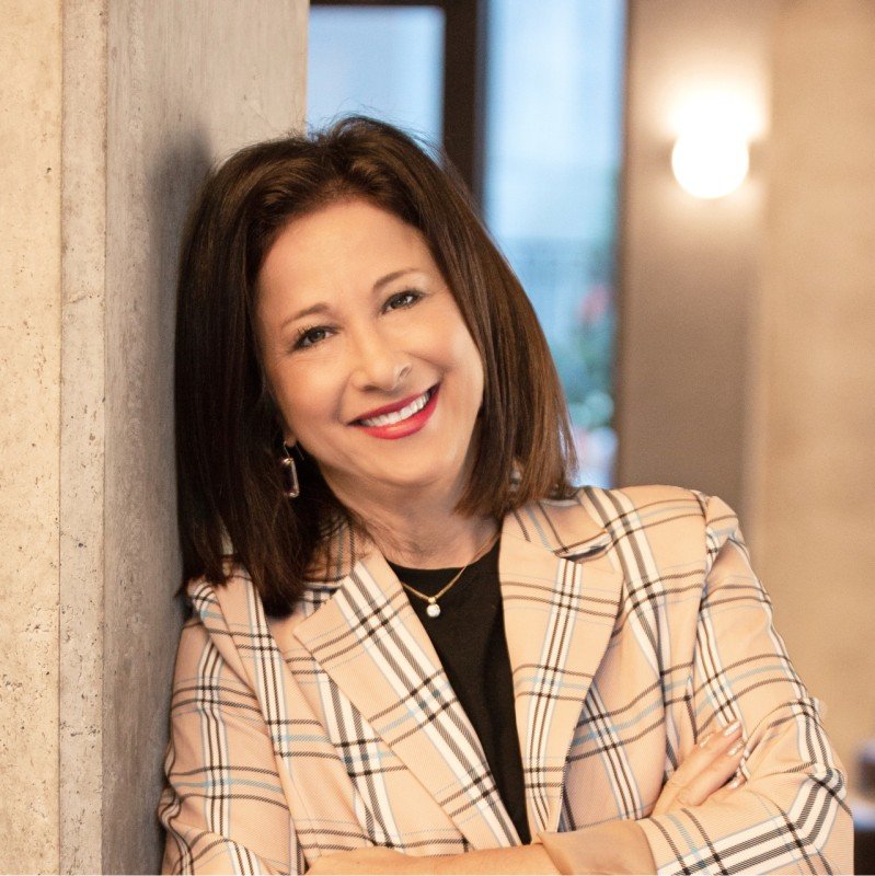 Julie Silard Kantor, Personal and Professional Life Coach at New York Intervention, smiling and leaning against a wall wearing a plaid blazer.