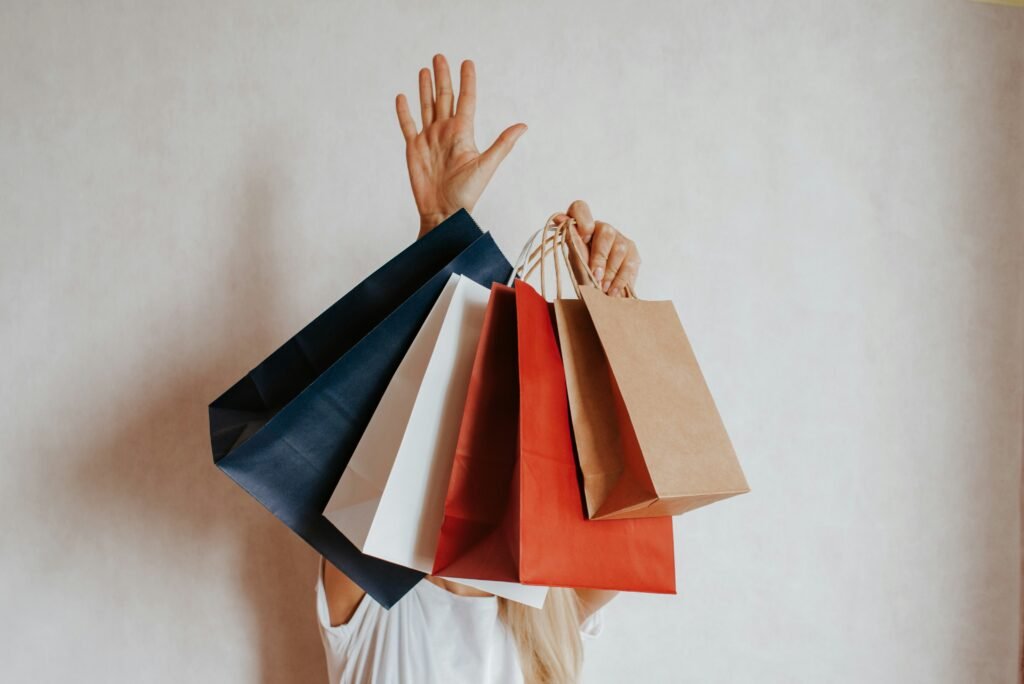 Person hidden behind a fan of shopping bags, representing compulsive spending and shopping addiction.