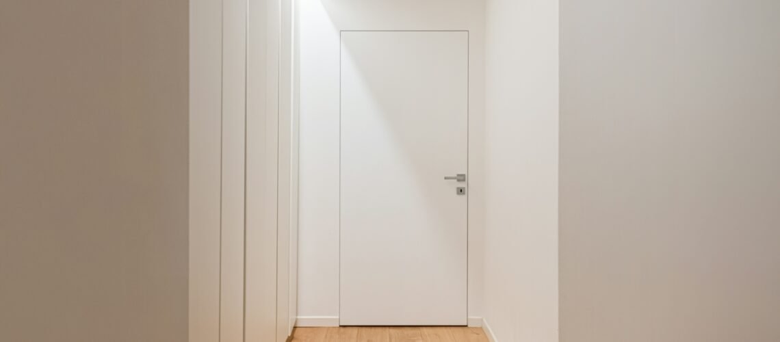 Closed door at the end of a quiet sunlit hallway, representing a young adult withdrawn during Failure to Launch