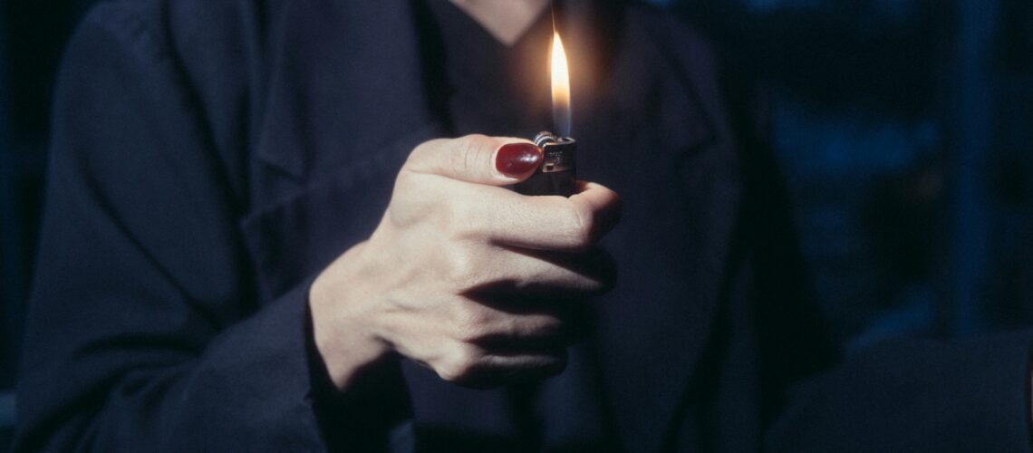 Hand holding a lit lighter at dusk, the flame illuminating the quiet, often-hidden moments of cannabis dependence.