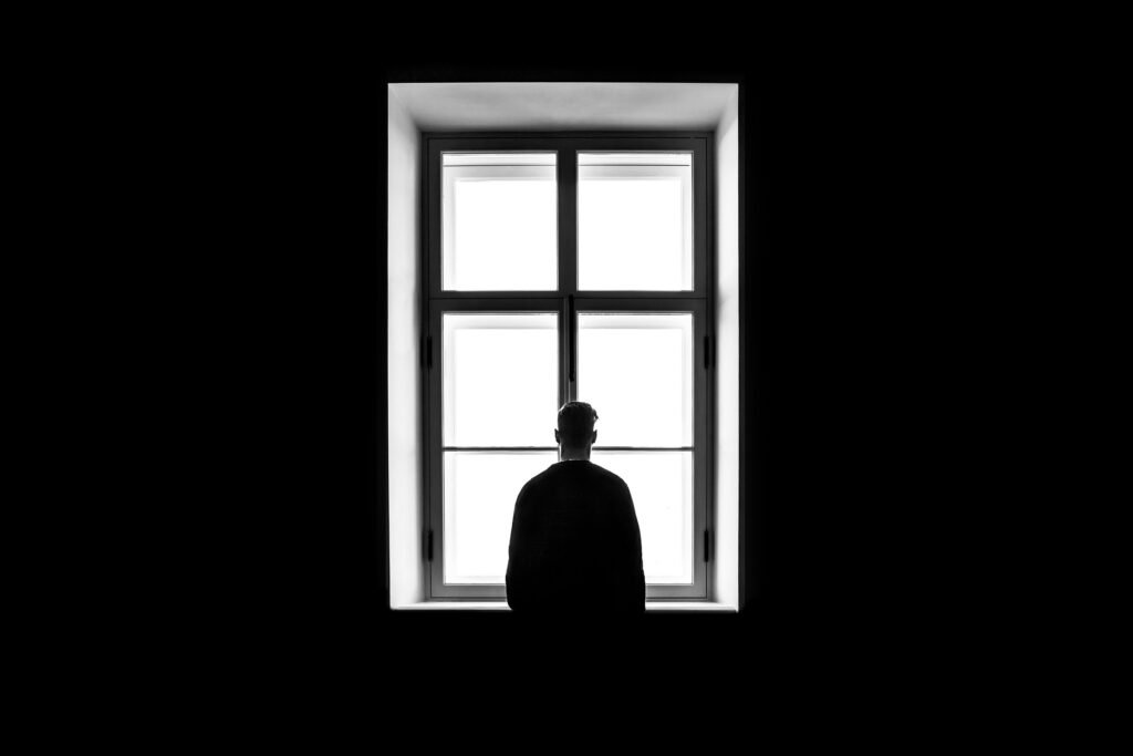 Silhouette of a person standing alone at a window in a dark room, illustrating the isolation and withdrawal often associated with marijuana addiction.