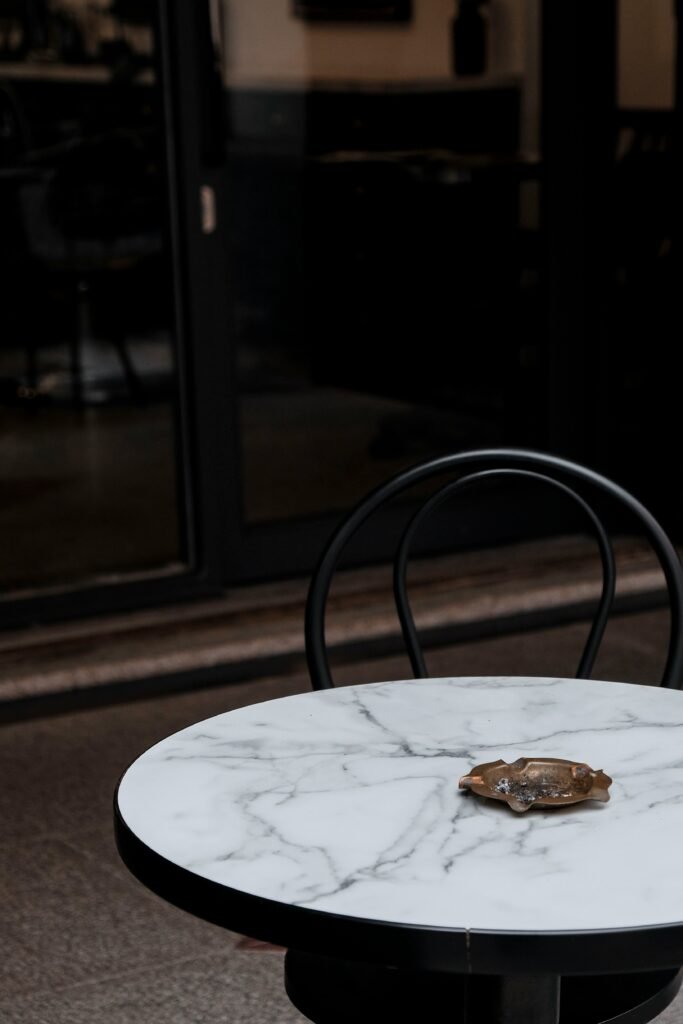 An empty chair beside a marble café table holding a worn ashtray, suggesting the quiet, solitary rituals that often accompany cannabis dependence.